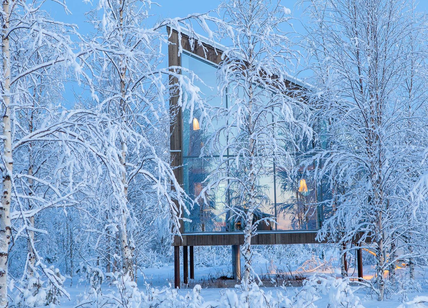 Bru & Bru agencia de viajes exclusivos - Arctic Bath Hotel Spa flotante en Laponia, Suecia. Exterior de cabaña de madera grande en la orilla del río en paisaje nevado