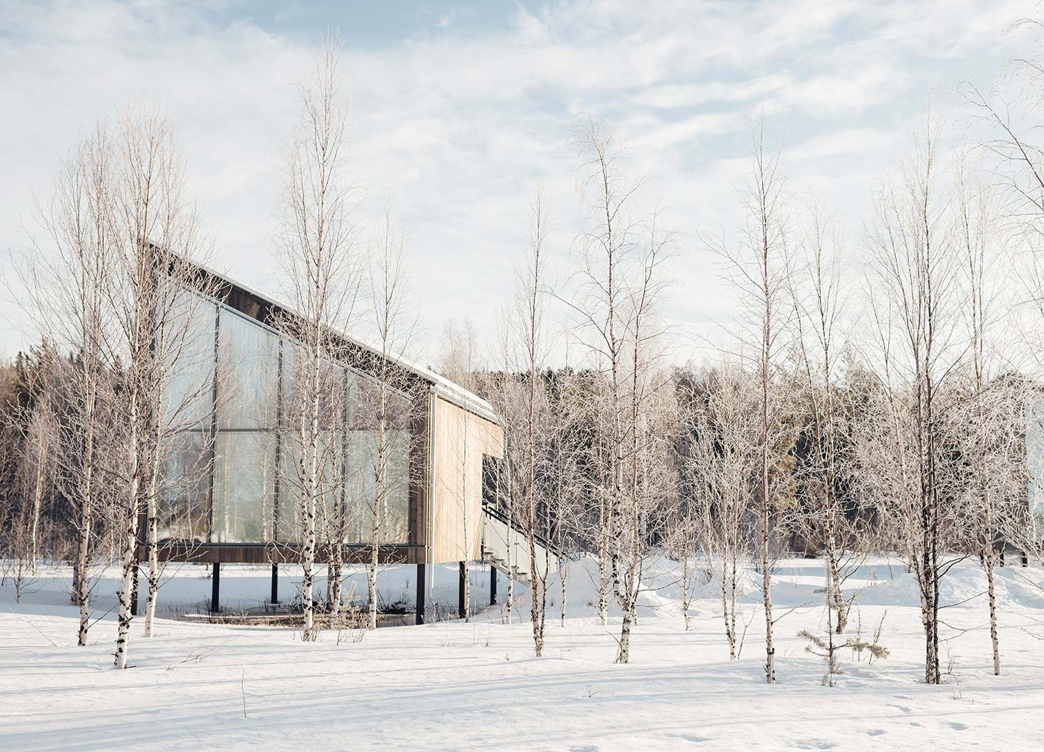 Bru & Bru agencia de viajes exclusivos - Arctic Bath Hotel Spa flotante en Laponia, Suecia. Exterior de cabaña de madera grande en la orilla del río en paisaje nevado